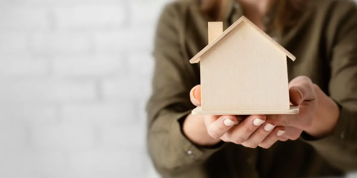 Handen houden een houten huisje vast – woning beschermen en verzekeren